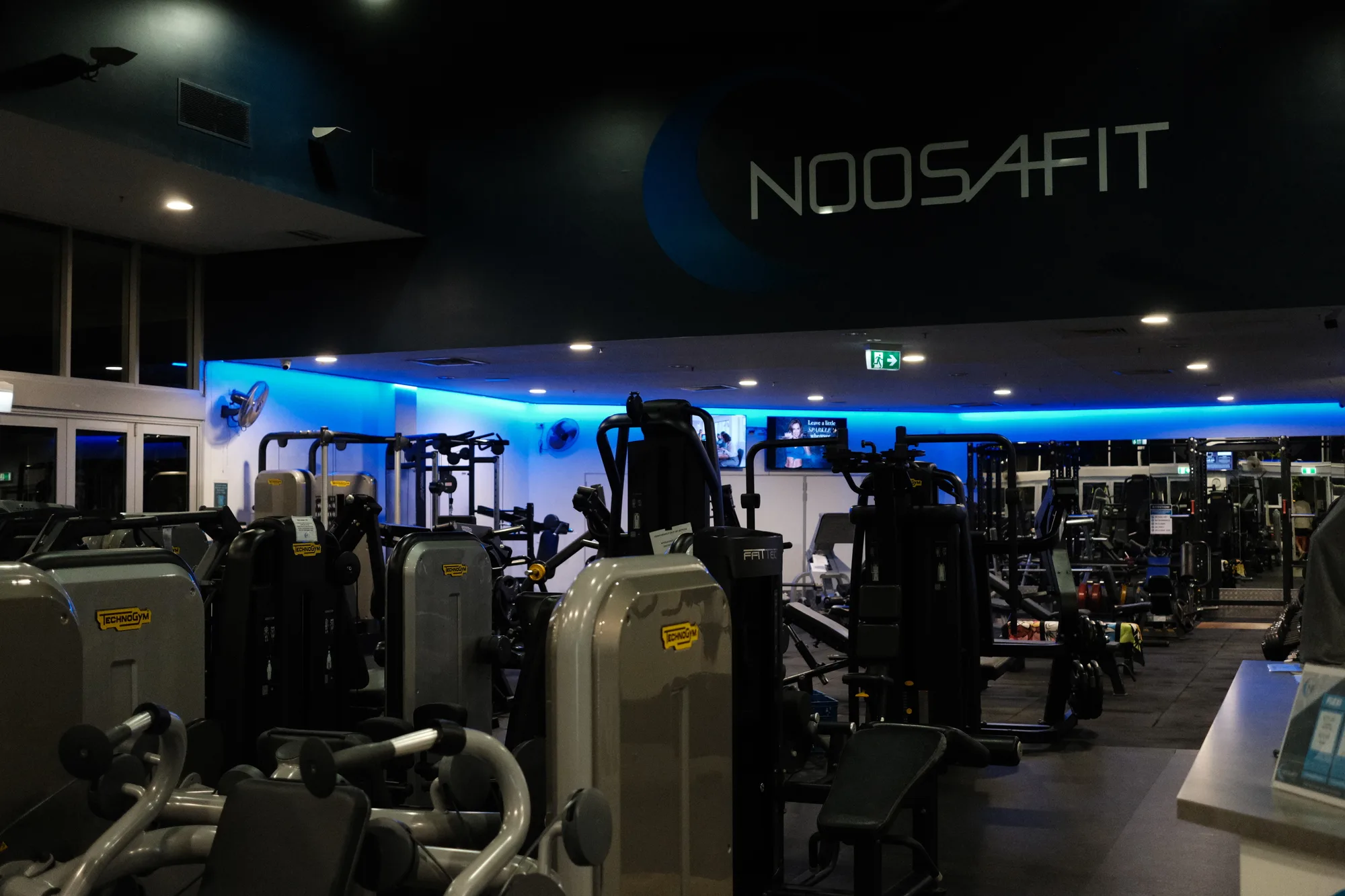 Gym floor with Technogym machines under the NoosaFit logo wall